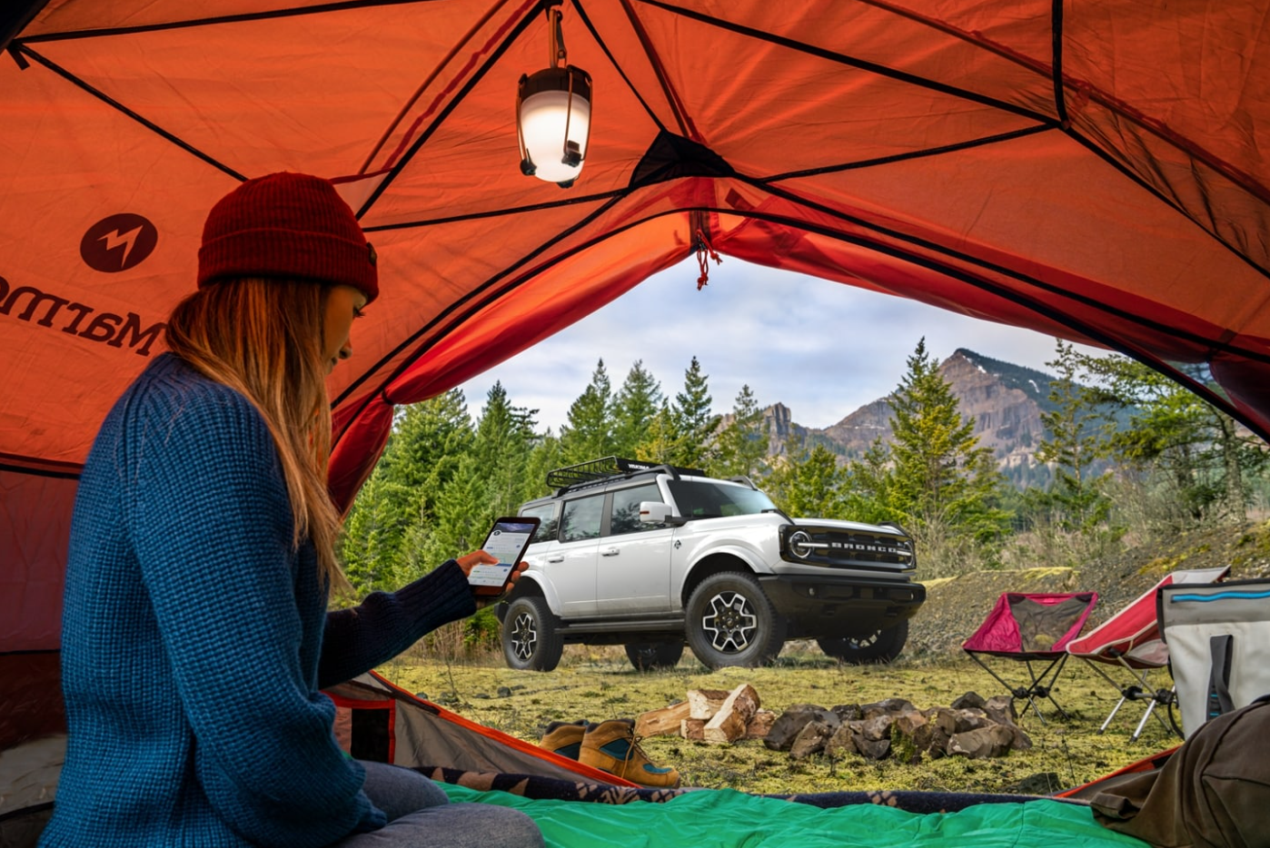 A view of a silver 2023 Ford Bronco parked at a campsite through the door of an orange tent.