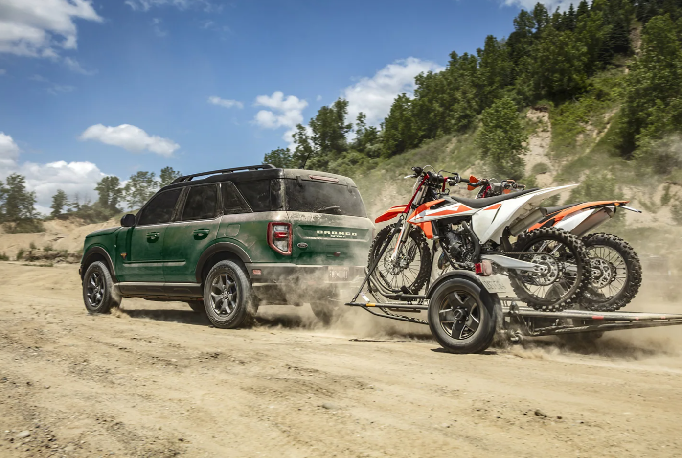 A dark green 2023 Ford Bronco Sport hauls a trailer of motorbikes