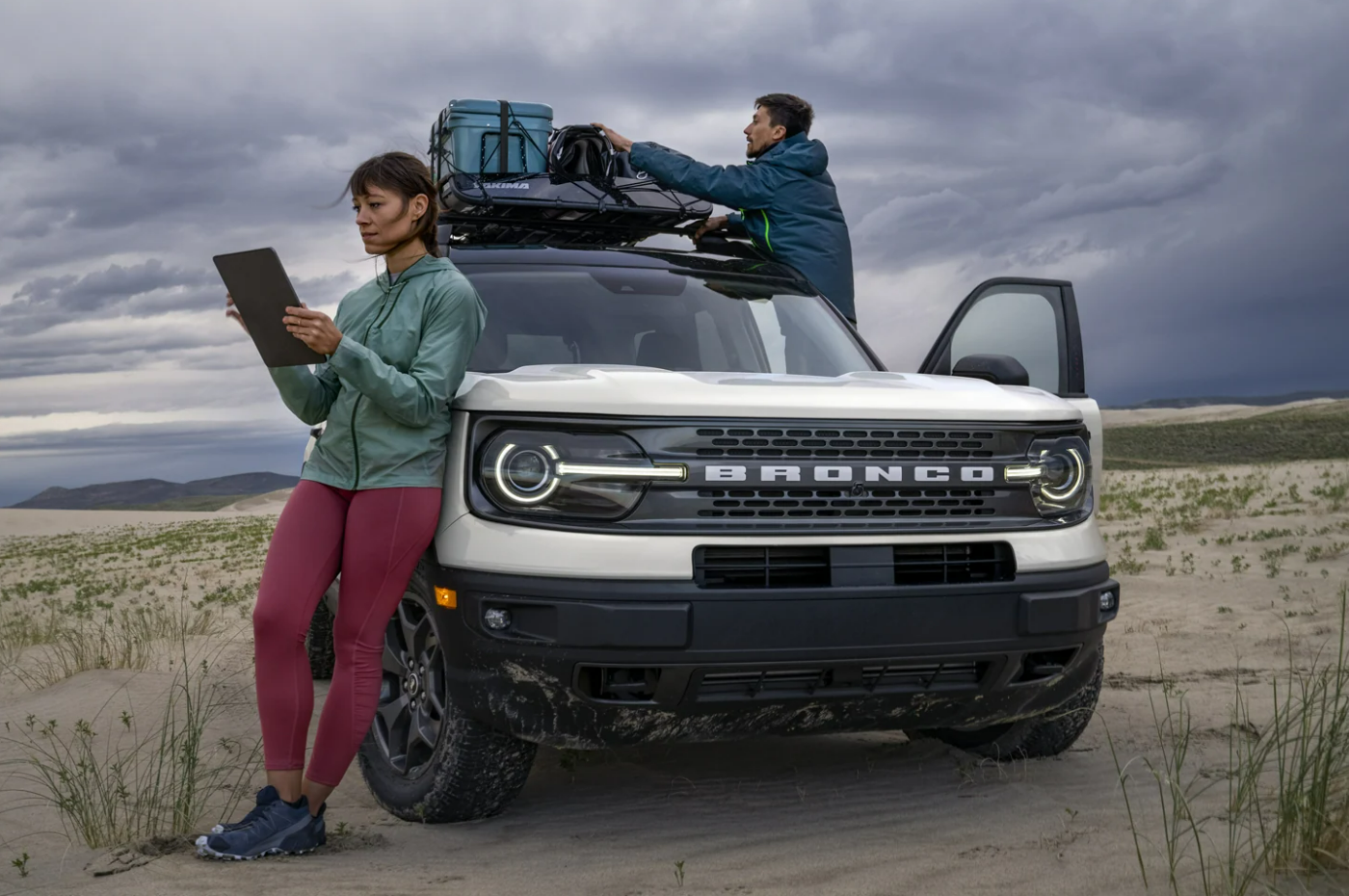 A woman leans against a white 2023 Ford Bronco Sport as a man takes cargo off the top of the car