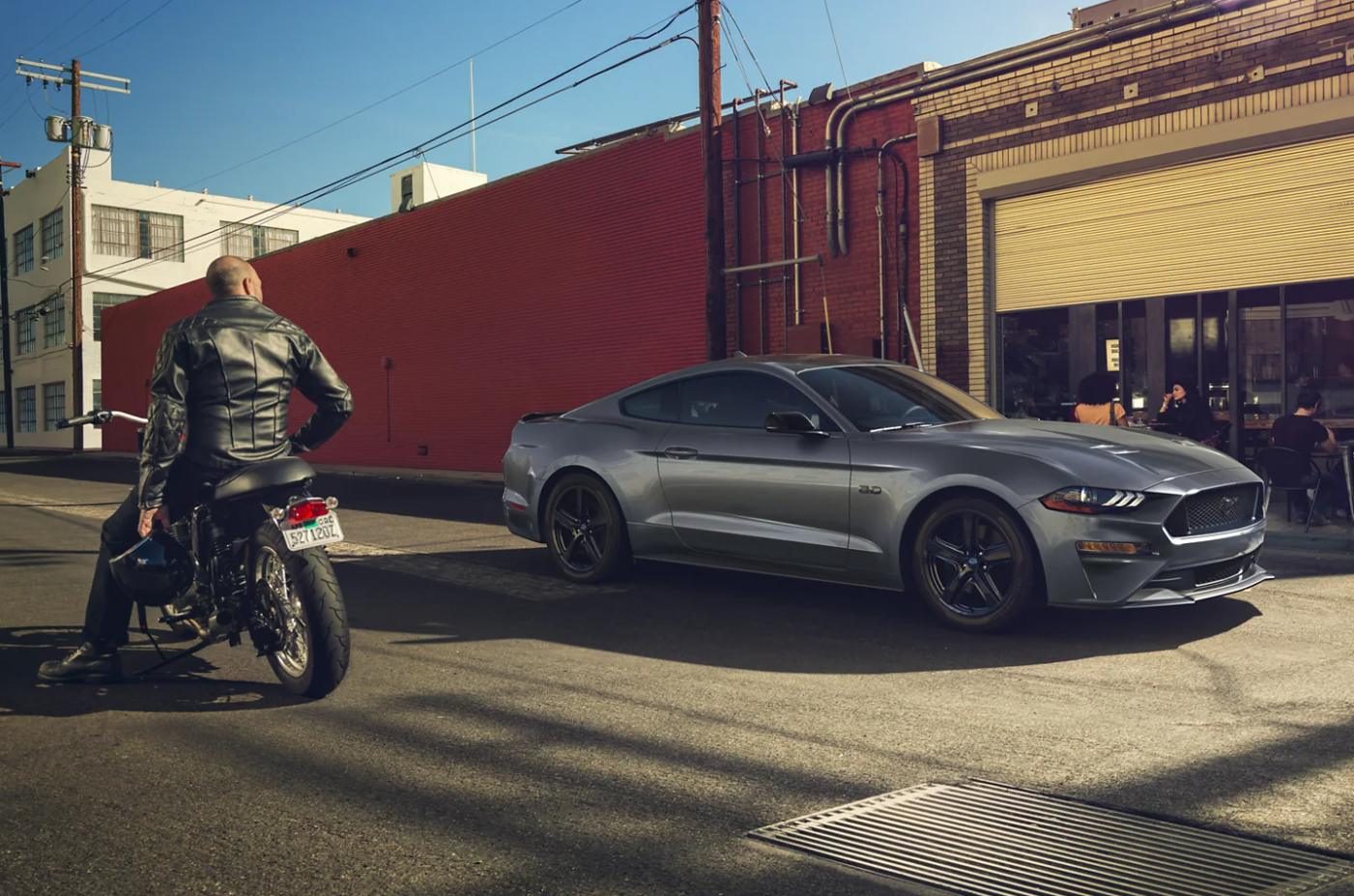 A gray 2023 Ford Mustang is parked on a city street next to a brick building