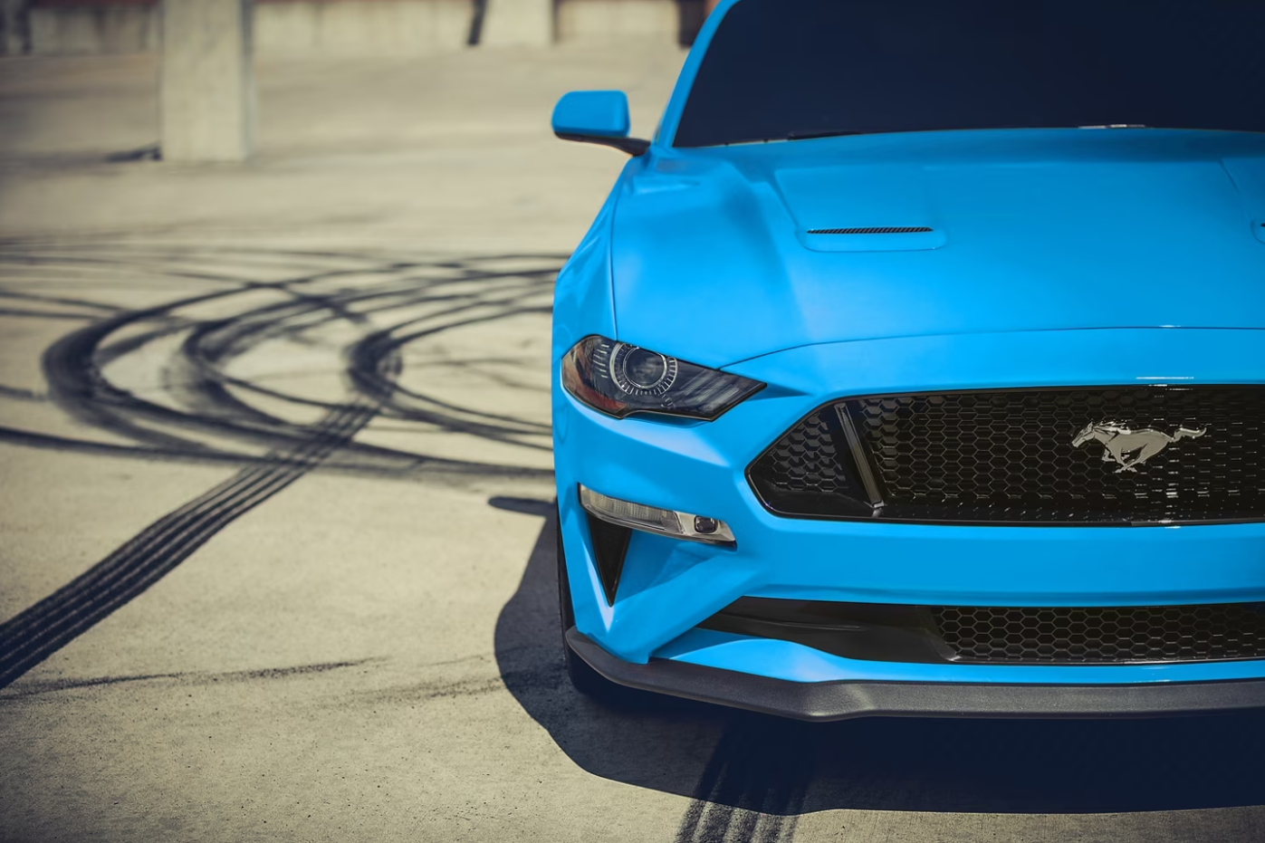 A view of the front of a bright blue 2023 Ford Mustang parked after leaving drag marks on asphalt